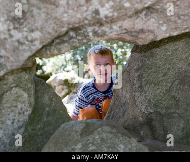 Un garçon, 5 ans, regarde avec curiosité à travers un tunnel de gros rochers Banque D'Images
