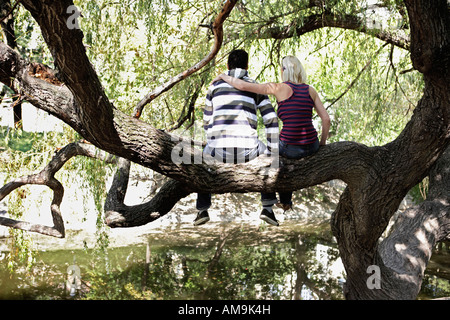 Couple assis dans un arbre par un lac. Banque D'Images