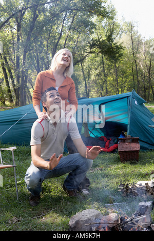 Couple de camping à la recherche jusqu'à la fumée du feu de camp en souriant. Banque D'Images