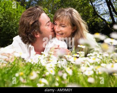 Couple allongé dans l'herbe en souriant et s'embrassant. Banque D'Images