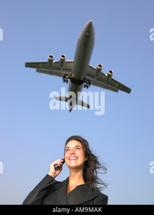 Femme sur téléphone cellulaire smiling avec avion volant au-dessus. Banque D'Images