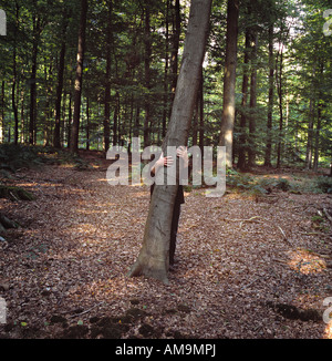 Un homme debout derrière un arbre avec les bras autour d'elle dans la forêt. Banque D'Images