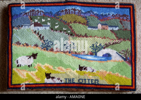 Prier à genoux genoux coussin prière culte broder point de croix coussin tissu rural rembourré champ scène pont rivière terre paysage moutons Banque D'Images