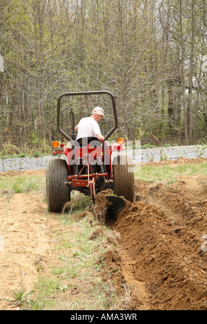 Homme conduisant un petit tracteur labourant ou labourer sur terrain ferme spécialiste Banque D'Images