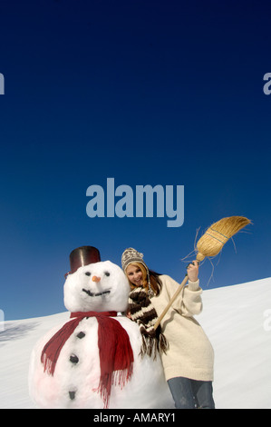 Young woman leaning on snowman, holding broom, low angle view Banque D'Images
