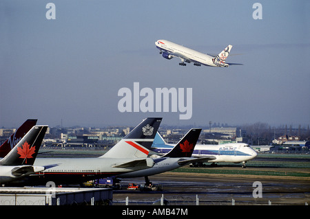 Aéroport d'Heathrow avec avions stationnés et un avion décollant en arrière-plan. Banque D'Images