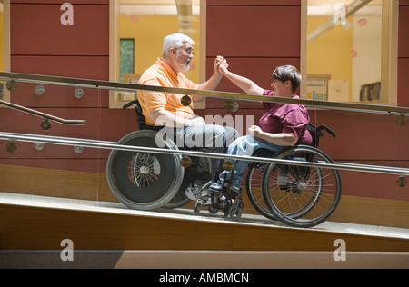 Profil de côté d'un homme d'âge moyen et une femme d'âge moyen assis en fauteuil roulant sur une rampe pour fauteuil roulant Banque D'Images