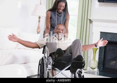 Femme d'âge moyen en poussant un homme d'âge moyen dans un fauteuil roulant et souriant Banque D'Images