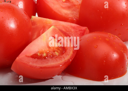 Gros plan de tomates rouges mûres biologiques entières et en morceaux section transversale d'au-dessus personne sur la table remplissant le fond avec des gouttes d'eau haute résolution Banque D'Images