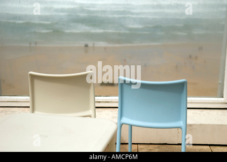 Deux chaises vides de l'arrière en regardant par la fenêtre plus nuageux avec plage surf à Cornwall Banque D'Images