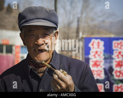 Homme édenté avec cap et pipe smiling outdoors Banque D'Images