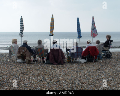 Un groupe de personnes âgées sur une journée assis ensemble à la plage de galets galets anticipe certains soleil parasol prêt ou peut-être la pluie Sussex England UK Banque D'Images