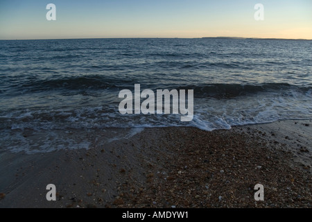 Petites vagues se brisant sur une plage de sable et de galets au coucher du soleil Banque D'Images