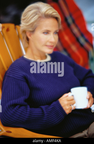 Mature Woman Sitting in Chair Holding Mug Banque D'Images