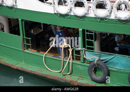 Un marin sur l'un des Star Ferries se prépare à lancer une amarre à un collègue sur le quai alors que le traversier quais à Kowloon Banque D'Images