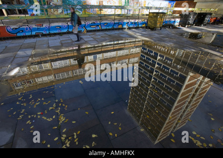 Une femme marche et un reflet dans une flaque d'un bloc d'appartements à Hoxton, East London Banque D'Images