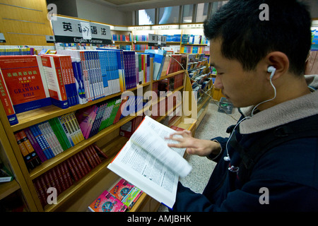 Les jeunes Chinois avec des écouteurs de la lecture d'un jeune homme chinois de langue anglaise avec des écouteurs de la lecture d'un livre en langue anglaise Banque D'Images