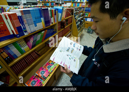 Les jeunes Chinois avec des écouteurs de la lecture d'un livre en langue anglaise, Beijing, Chine Banque D'Images