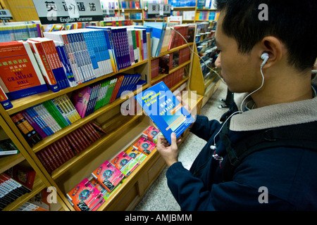 Les jeunes Chinois avec des écouteurs de la lecture d'un livre en langue anglaise, Beijing, Chine Banque D'Images