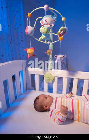 Un bébé est sur le dos sur un lit bébé et regarde un mobile dans une pépinière de nuit Banque D'Images