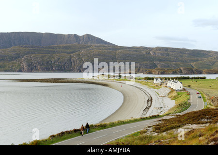 Ardmair village près d'Ullapool, Wester Ross, Scotland. Couple en train de marcher le long de la route côtière en direction de maisons de vacances au-dessus de plage de galets. Banque D'Images