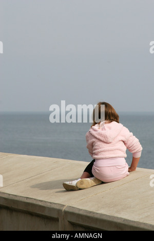 Fille assise sur le nouveau mur de défense de la mer de béton à Scarborough. Banque D'Images