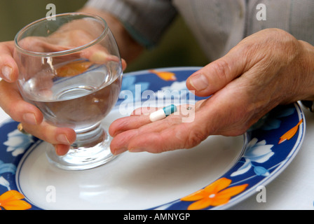 Mains d'une vieille femme tenant un comprimé et un verre d'eau Banque D'Images