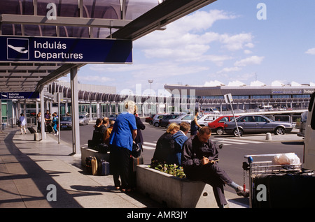 L'aéroport international terminal 2B bâtiment avec des passagers assis à l'extérieur d'attente ci-dessous les départs signe. Budapest Hongrie Banque D'Images