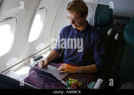 L'homme de race blanche d'âge moyen à l'aide d'un ordinateur portable assis dans un avion en classe affaires Banque D'Images