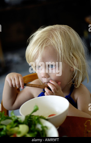 Alimentation bébé fille elle-même sur une chaise haute à l'aide d'une cuillère. 2007 Banque D'Images