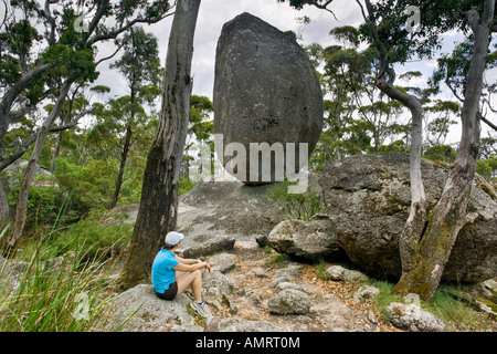 Une jeune femme était assise à l'atteinte d'un équilibre entre rock, un énorme bloc de granite dans l'ancien parc national de Porongurup, Australie occidentale Banque D'Images