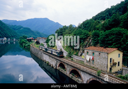 Un train passe le long du côté de la rivière Serchio près de Borgo a Mozzano en Italie. Banque D'Images