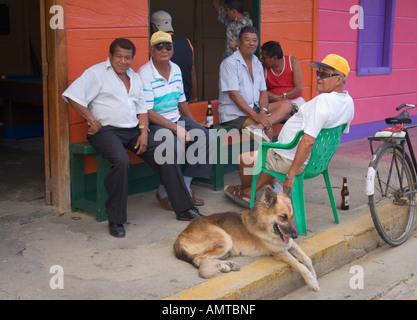 Groupe d'hommes et un chien assis dehors bénéficiant d'un magasin d'alcool de la bière dans la ville portuaire de San Juan del Sur République du Nicaragua Banque D'Images