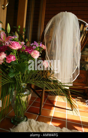 Bridal Veil accroché au dos ou une chaise à côté de fleurs et de verdure dans un vase debout sur un sol carrelé highligted avec sunshine Banque D'Images