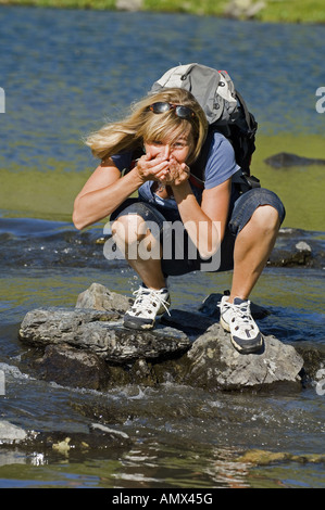 Femme buvant de l'eau pure de montagne, Alpes, France Banque D'Images