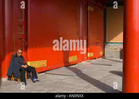 Chine Beijing Dongcheng La Cité Interdite Chineese homme assis sous une véranda à côté d'énormes portes wodden peint rouge Banque D'Images