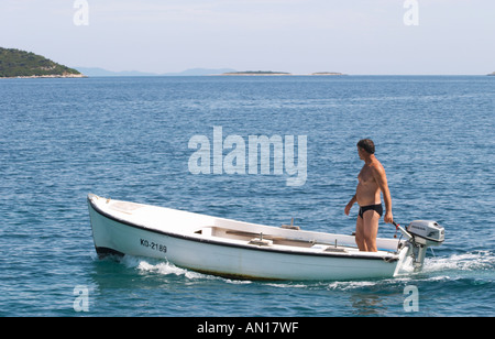 Un homme debout, dans un petit bateau avec un moteur hors-bord Honda sur le bleu de la mer, des îles dans l'arrière-plan Orebic ville, station balnéaire sur la côte sud de la péninsule de Peljesac. Orebic ville. Péninsule de Peljesac. La côte dalmate, en Croatie, en Europe. Banque D'Images