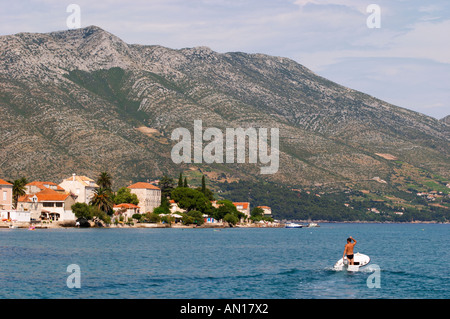 Un homme debout, dans un petit bateau avec un moteur hors-bord Honda sur le bleu de la mer, dans l'arrière-plan les massifs montagneux de la péninsule de Peljesac et le village Mont mont. Orebic ville, station balnéaire sur la côte sud de la péninsule de Peljesac. Orebic ville. Péninsule de Peljesac. La côte dalmate, en Croatie, en Europe. Banque D'Images