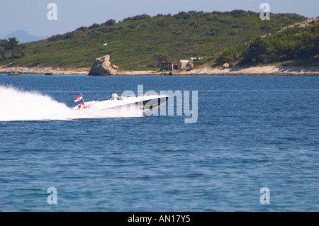 Un hors-bord bateau de vitesse en haut débit à travers l'eau avec du blanc jet avec la Suisse et croate de drapeaux et d'une île à l'arrière-plan Orebic ville, station balnéaire sur la côte sud de la péninsule de Peljesac. Orebic ville. Péninsule de Peljesac. La côte dalmate, en Croatie, en Europe. Banque D'Images