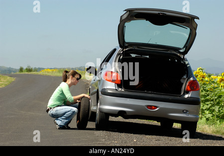 Femme avec un pneu à plat sur sa voiture de changer la roue garé au bord de la route dans le pays Banque D'Images