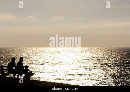 Deux personnes assis sur un banc regardant le coucher de soleil sur Cornwall Banque D'Images