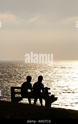 Deux personnes assis sur un banc regardant le coucher de soleil sur Cornwall Banque D'Images