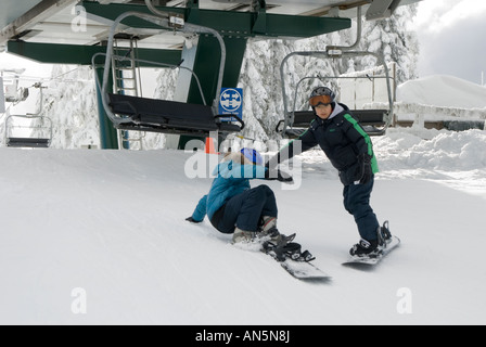 Les enfants sur les planches de descendre d'un télésiège Banque D'Images