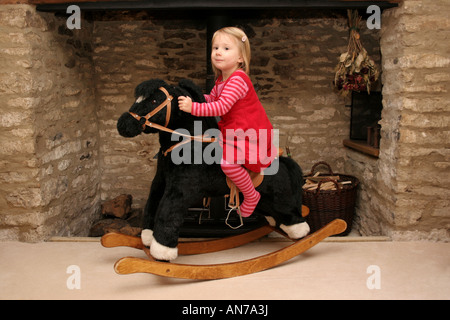 Le portrait d'une fillette de 4 ans sur un cheval à bascule en face d'une cheminée à foyer ouvert. Banque D'Images