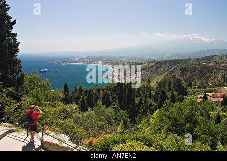 Un touriste vêtu de rouge prend une photo en regardant vers le sud le long de la côte de la mer Méditerranée le volcan Etna fume paisiblement Banque D'Images