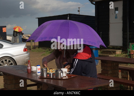 Mer pluie Royaume-Uni, homme femme abritant sous un parapluie mangeant du poisson et des frites dans la pluie Bank Holiday lundi, années 2006 2000 Angleterre HOMER SYKES Banque D'Images