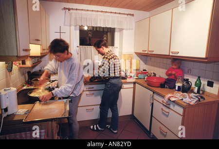 Père et mère à préparer le dîner avec enfant assis sur un évier de cuisine dans des ménages européens Banque D'Images