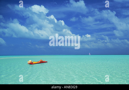 Woman floating in paradise sur matelas d'air entre les eaux aqua et les nuages blancs avec voilier sur l'horizon. Maison de vacances pittoresque. Banque D'Images