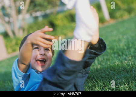 3 ans de race blanche mixte garçon asiatique hispanique avec ses pieds en l'air sur l'herbe Banque D'Images