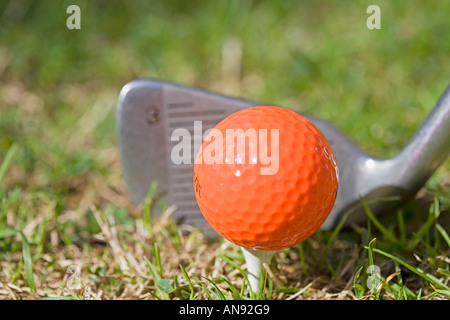 Frappant un coup de fer 3 sur une balle de golf orange tee en bois Banque D'Images